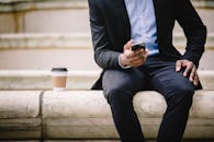 咖啡休息期间，一位穿着正式服装的无脸男性经理坐在大理石长凳上用手机发信息