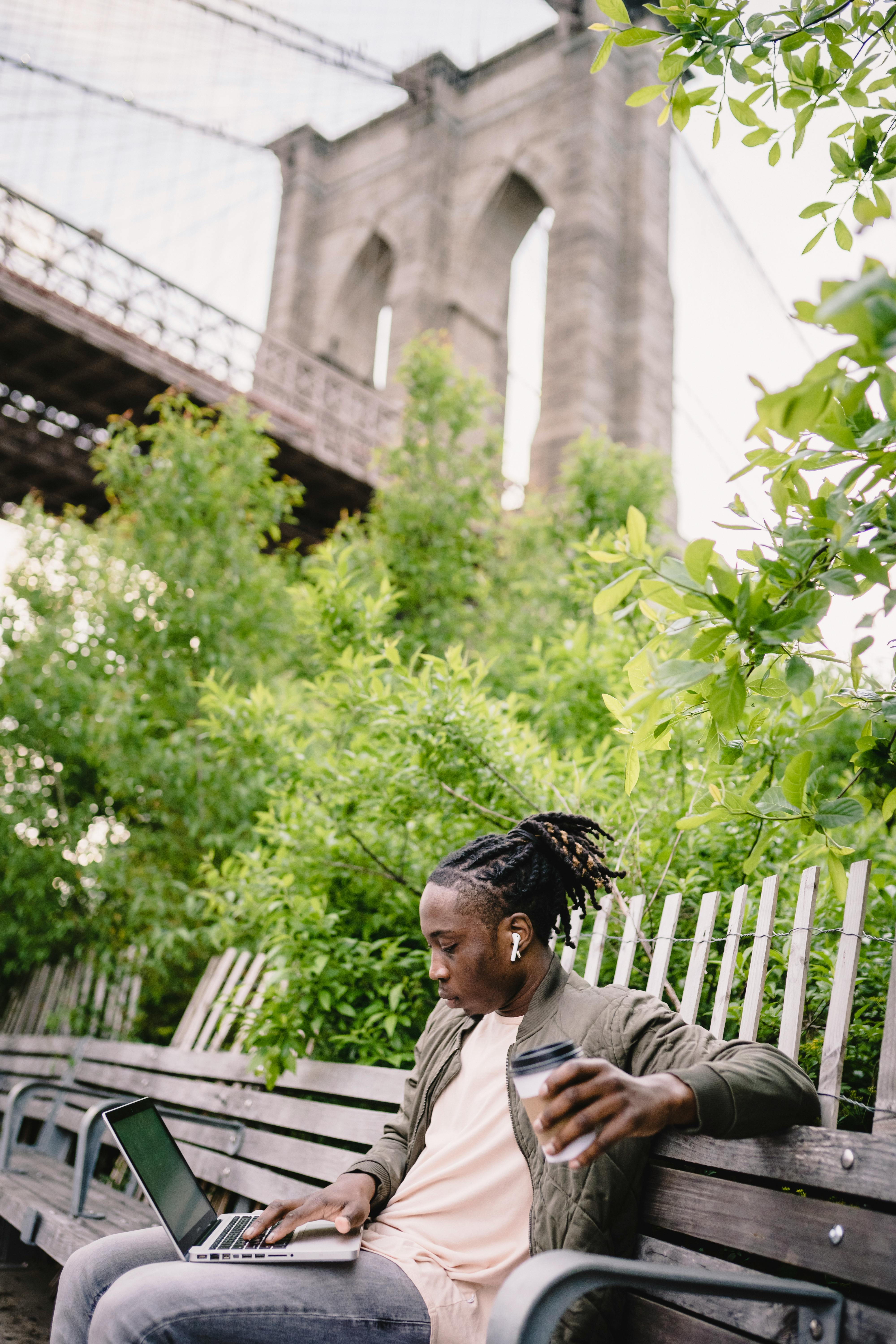 pensive black man with takeaway coffee entertaining with laptop in park