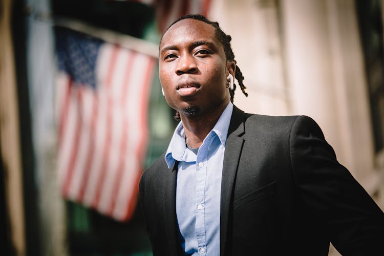 Serious Black Businessman Against Blurred Building With American Flags