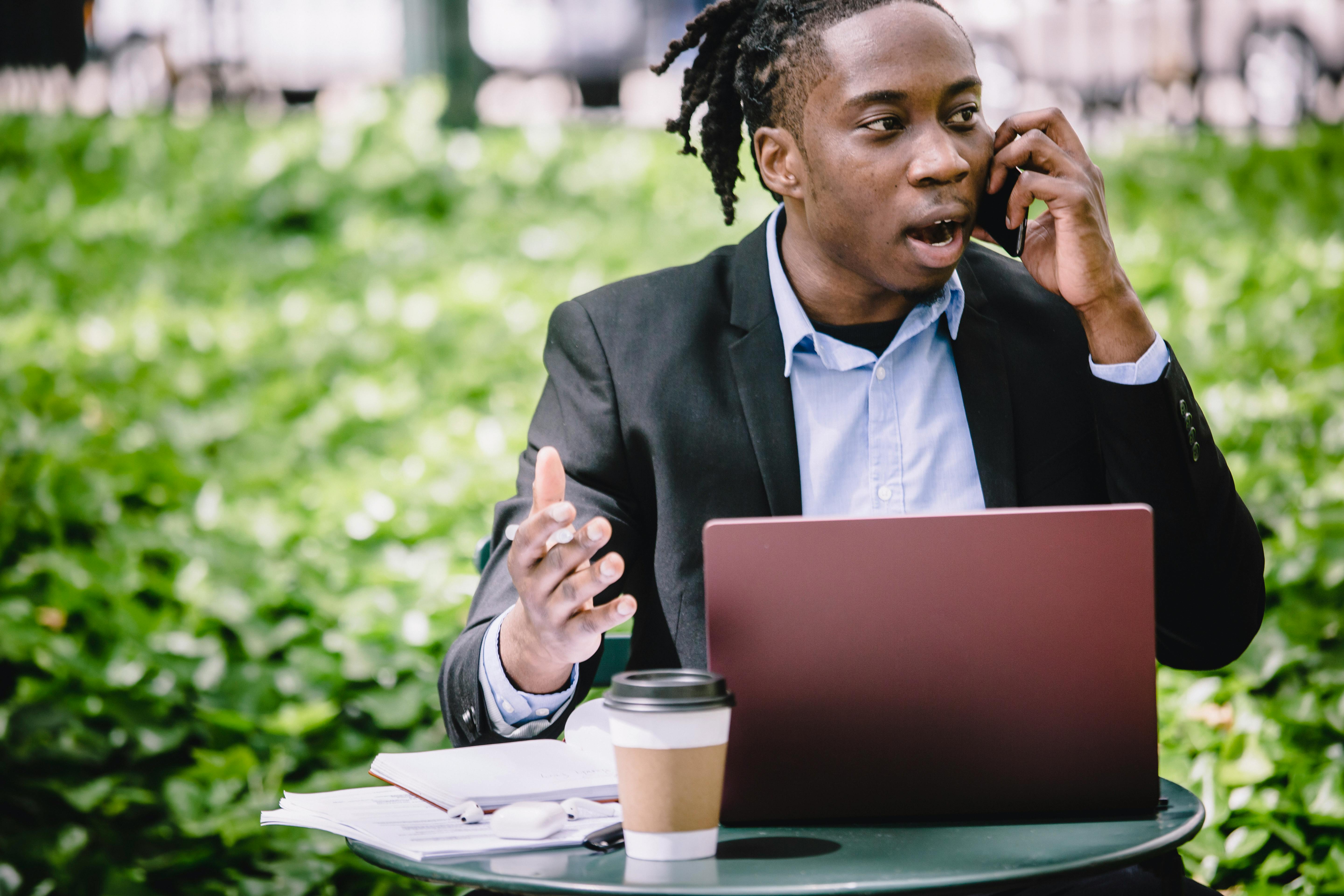 young businessman with laptop arguing on smartphone in street cafe