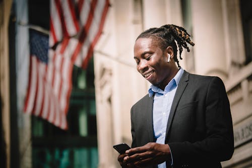 Free Positive young black entrepreneur using mobile on street and smiling Stock Photo