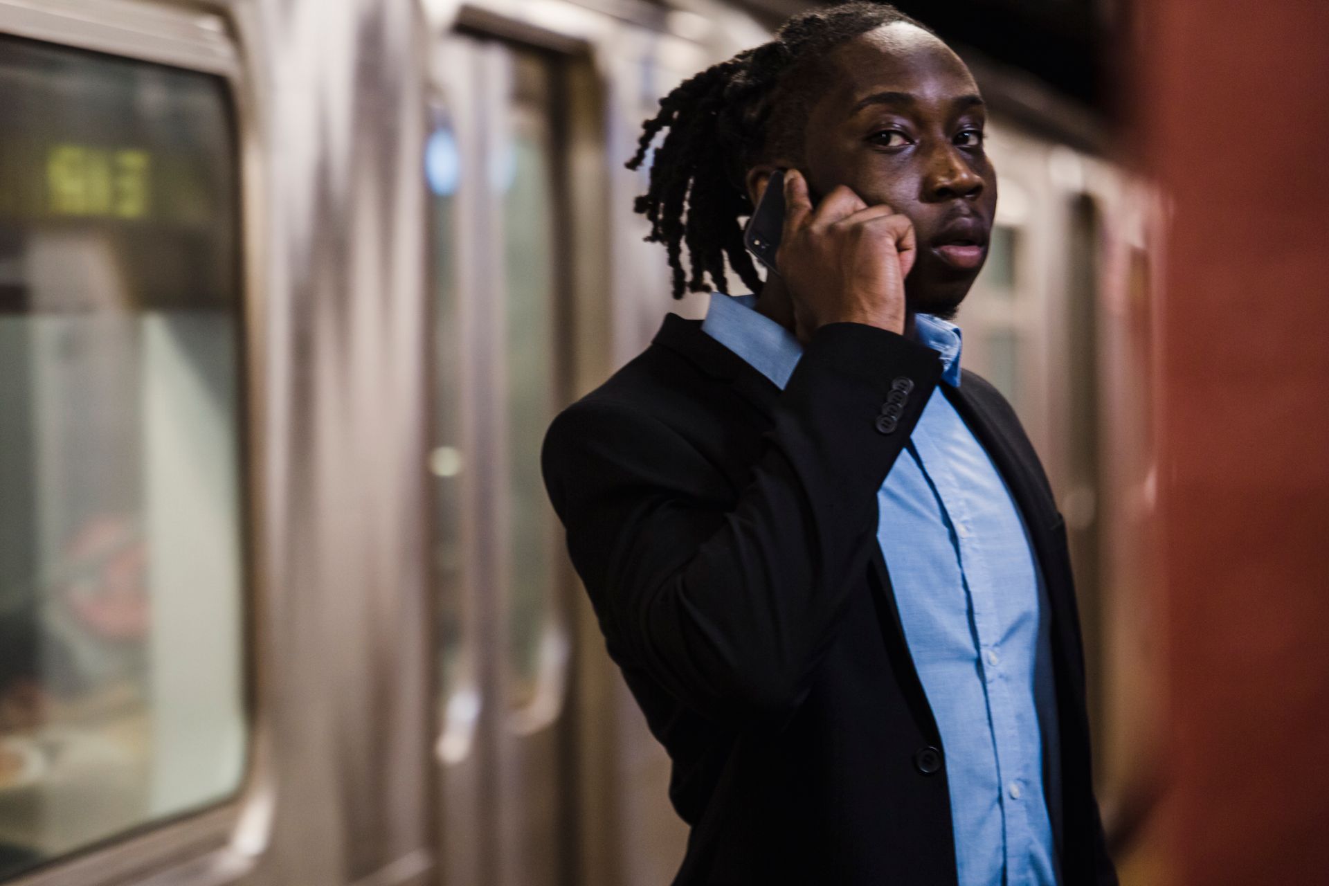 Young African American office worker in formal suit making phone call while standing in subway and waiting for train