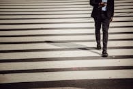 Faceless businessman with smartphone walking on crosswalk in sunlight