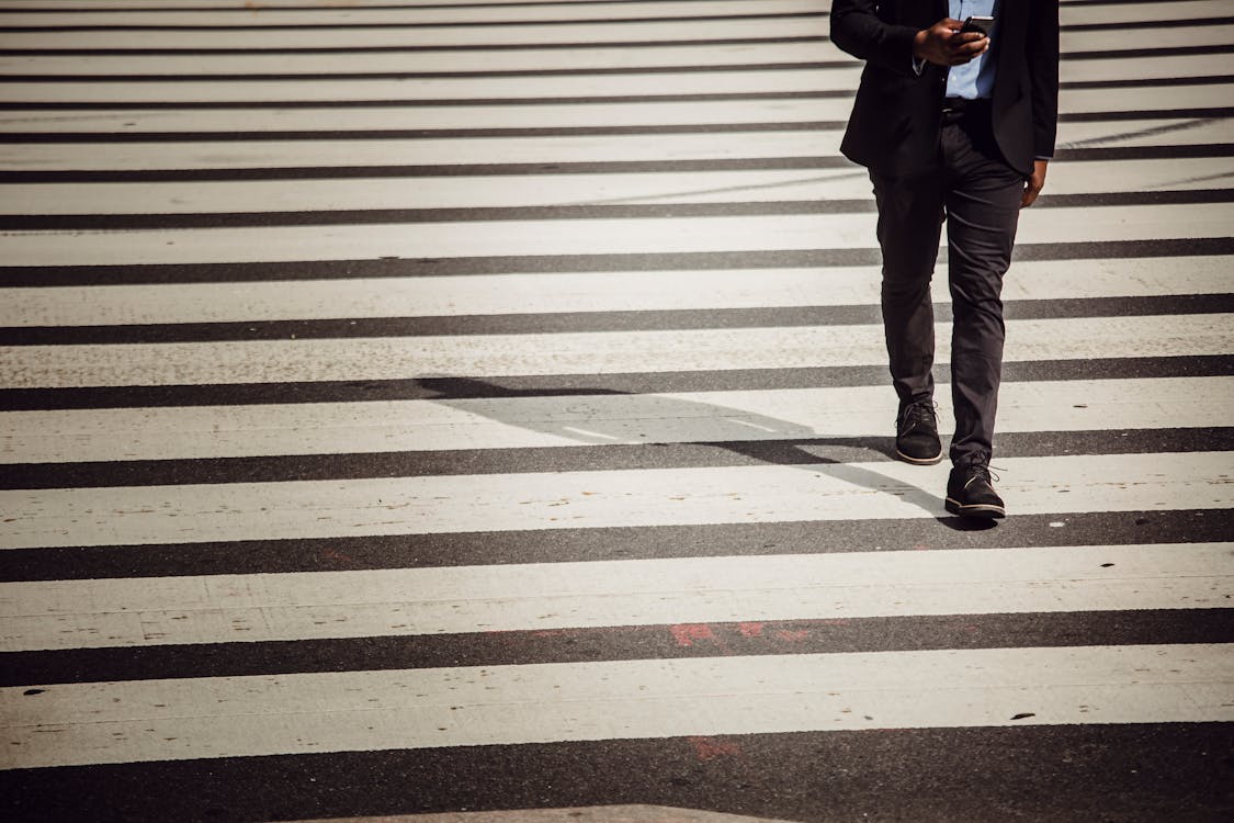 Free Faceless businessman with smartphone walking on crosswalk in sunlight Stock Photo