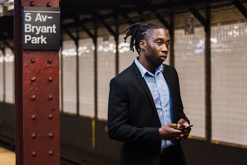 Confident male in office suit with mobile waiting for train