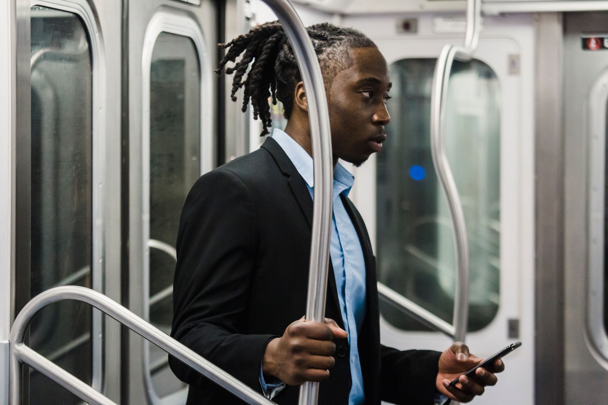 Side view of young pensive African American male in formal wear with mobile in hand standing near grab rail while commuting home from work by metro train