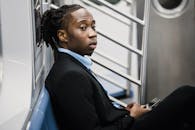 留着辫子的时尚年轻人在地铁列车上使用智能手机