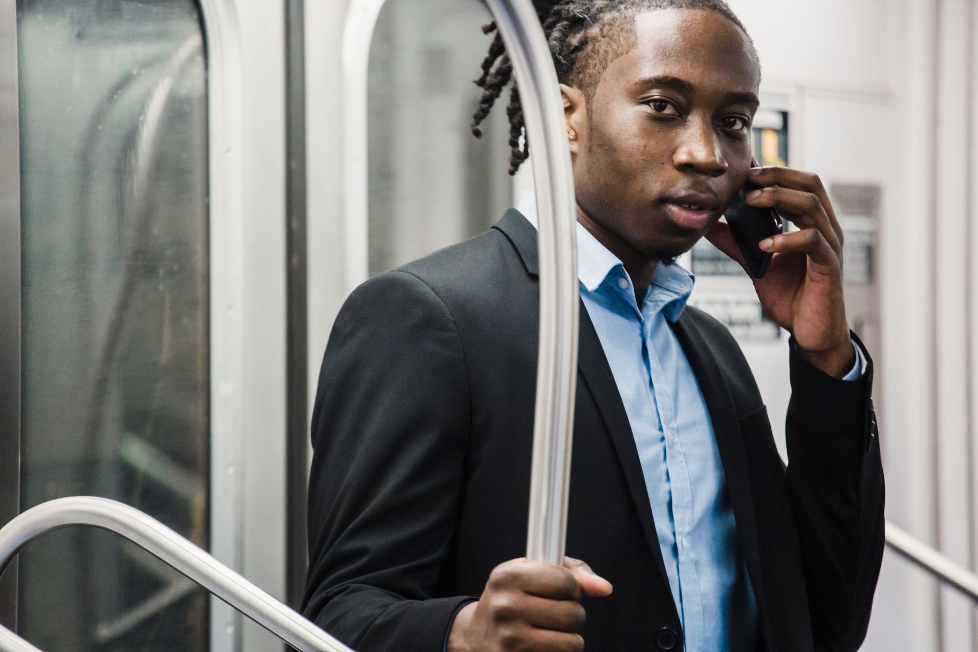 Young handsome African American male in formal suit making phone call on smartphone while traveling by commuter train