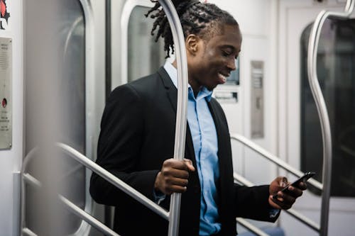 Free Cheerful black man surfing net on mobile on subway train Stock Photo