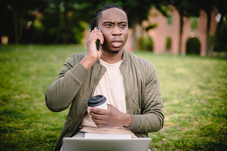 Young Black Man With Coffee Talking On Phone And Frowning