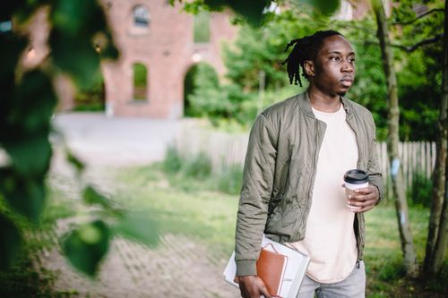 Free Serious young black student with dreadlocks in ponytail with coffee to go and notebooks spending time in green park Stock Photo