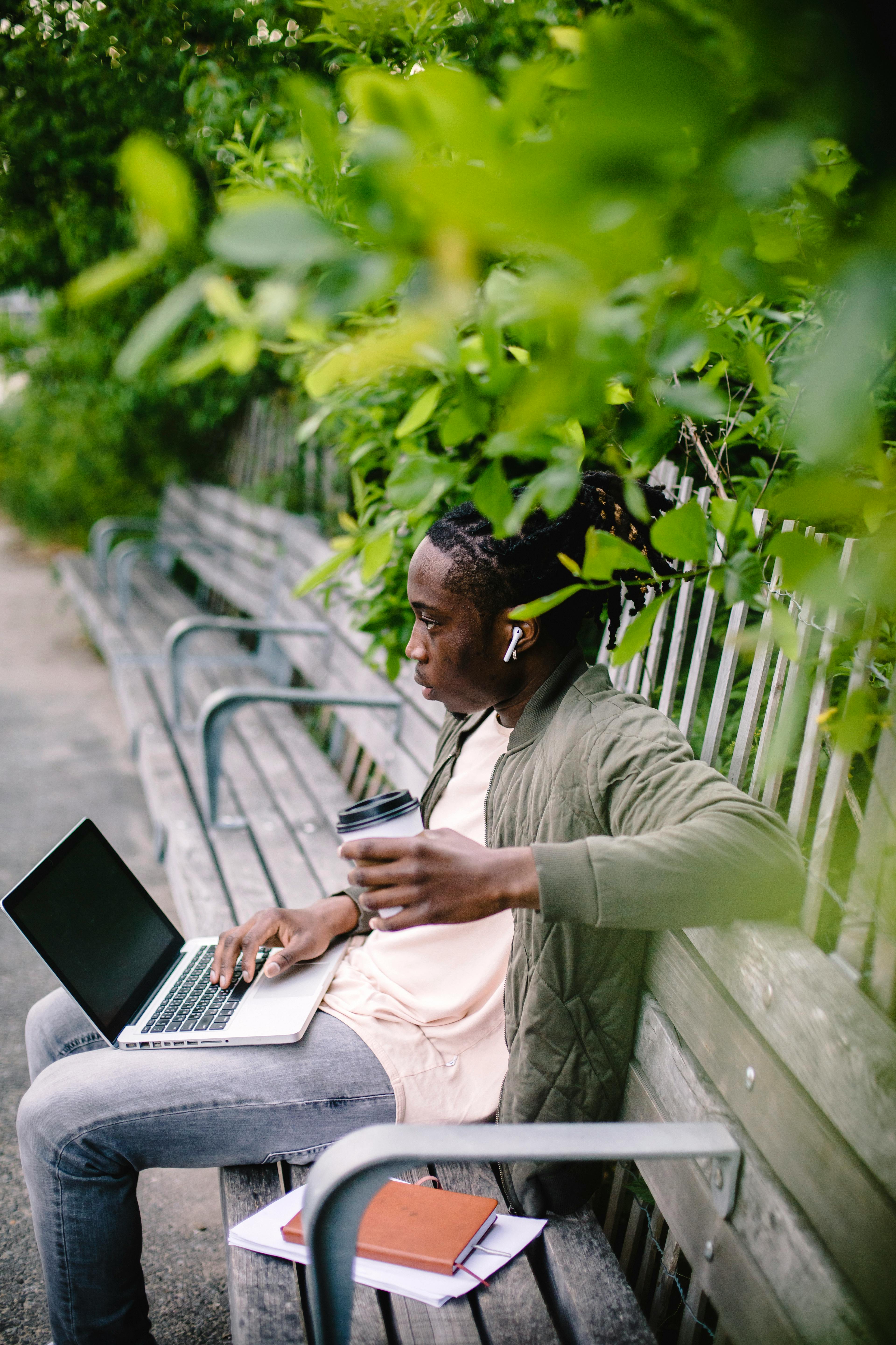 wistful man with coffee and laptop relaxing on park bench