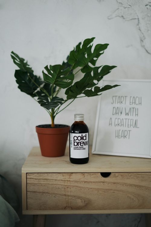 Free A cold brew coffee bottle on a wooden table with a potted plant and motivational quote. Stock Photo
