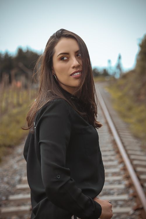 Free A fashionable young woman in black poses confidently on railway tracks, showcasing beauty and style. Stock Photo