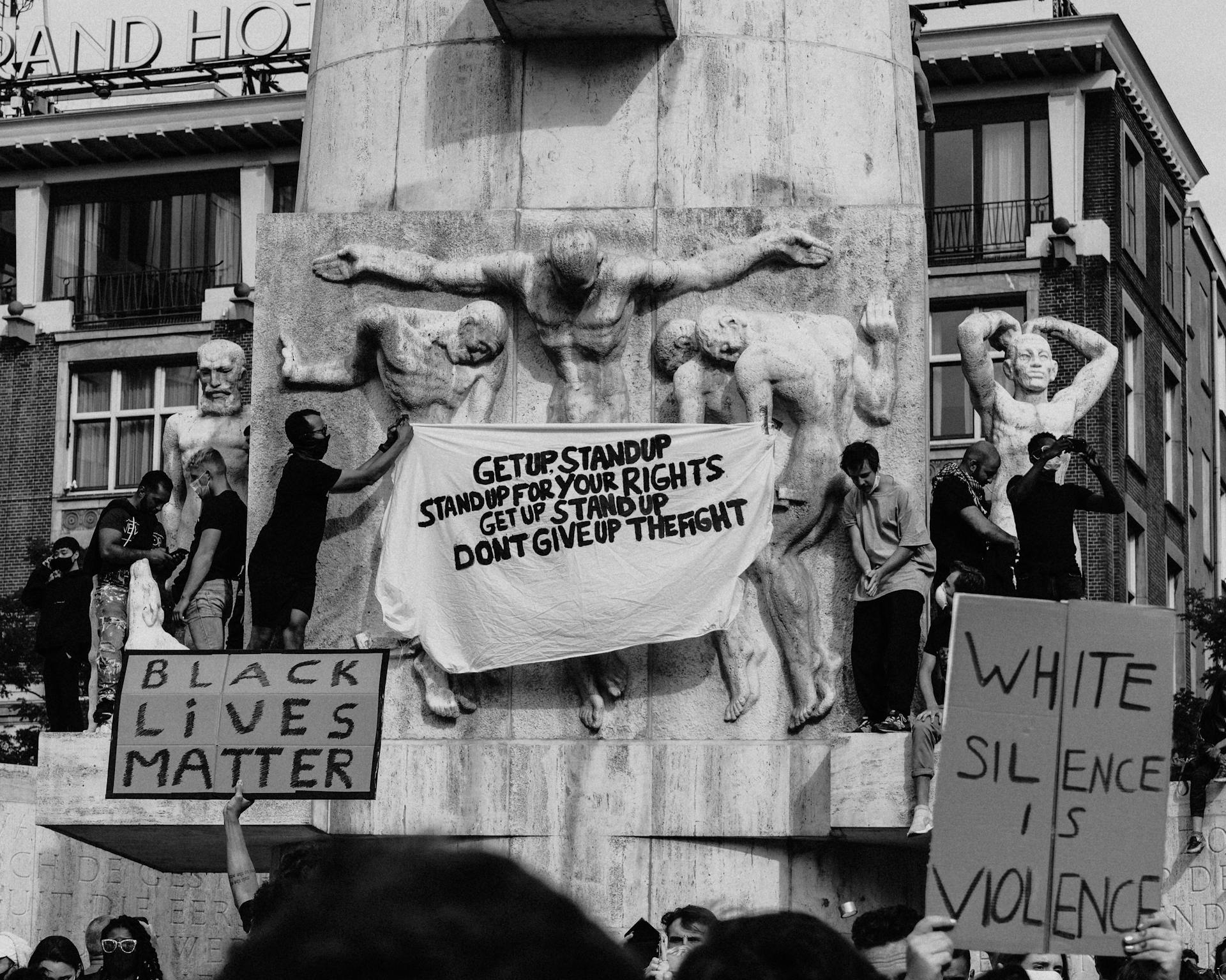 Black and white of crowd of people standing on city street with carton boards during social protest