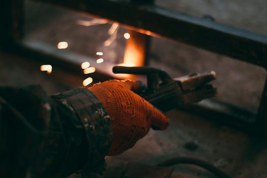 Detailed shot of a gloved hand holding an electrode holder during welding, sparks flying.