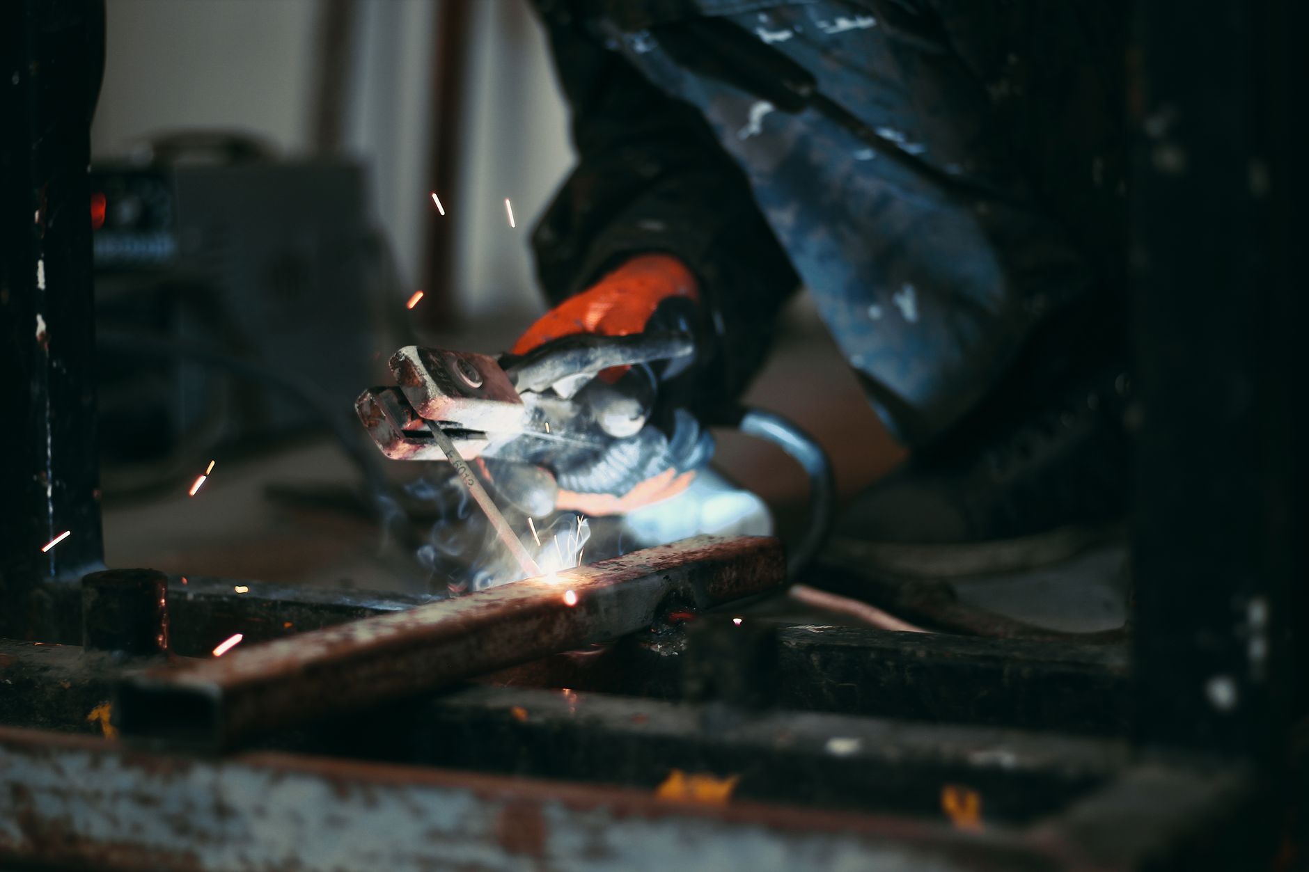 Focused shot of a welder's hands holding an electrode while sparks fly during metalwork.