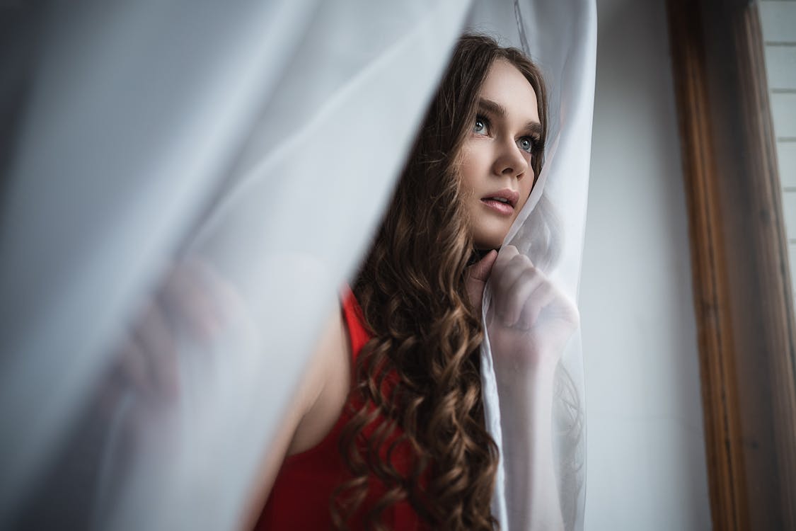 Free Thoughtful young woman standing near curtains Stock Photo