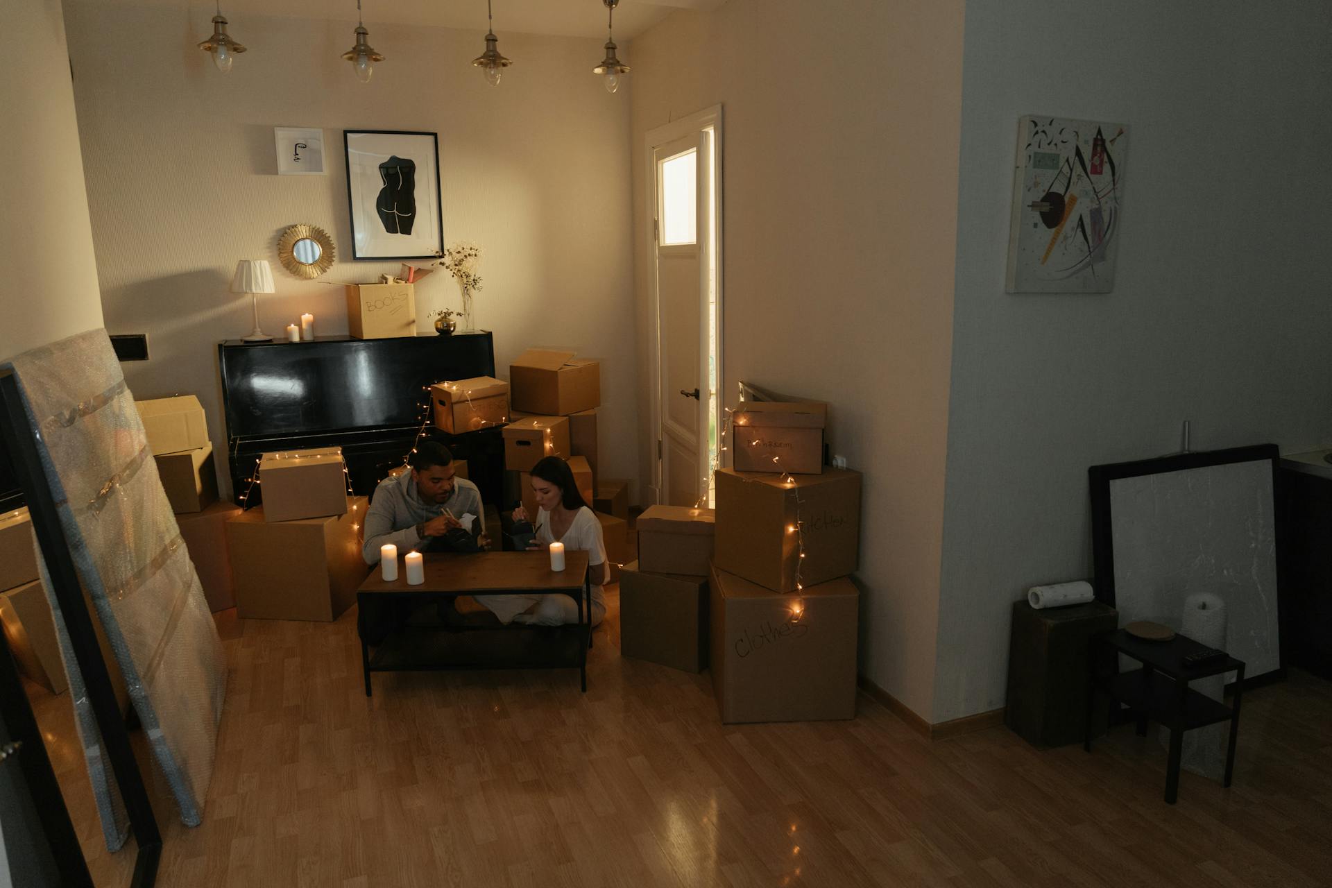 A couple enjoys a cozy moment amidst moving boxes, lit by candles in their new home.