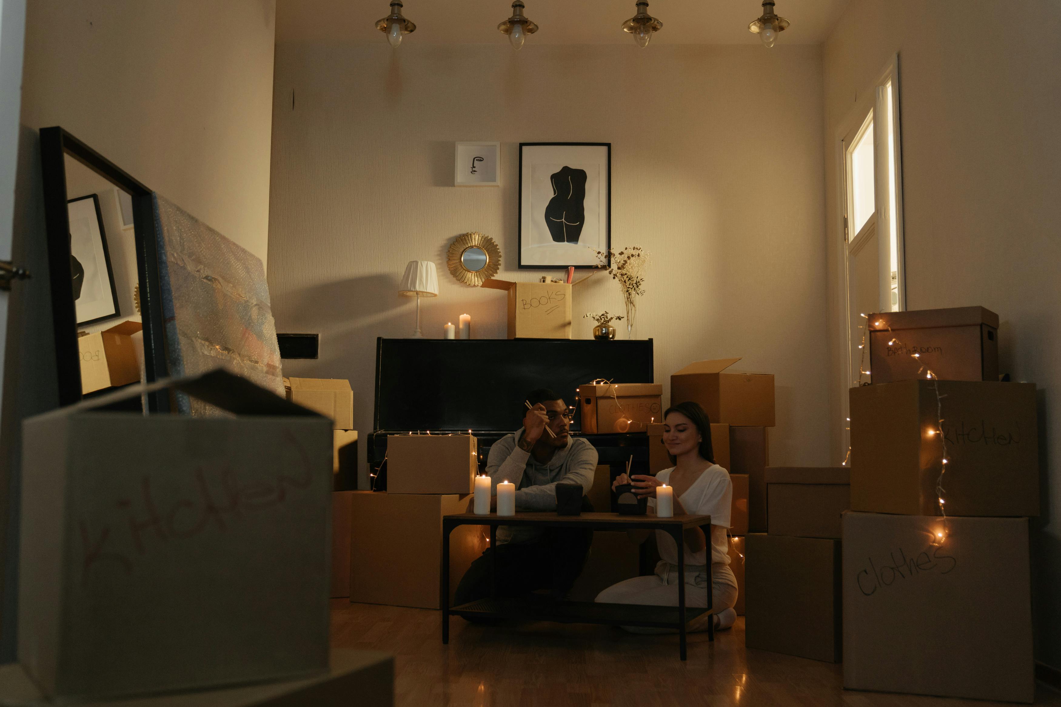 一对夫妇搬家时，在一个装满盒子的房间里，周围点着蜡烛，灯光温馨舒适