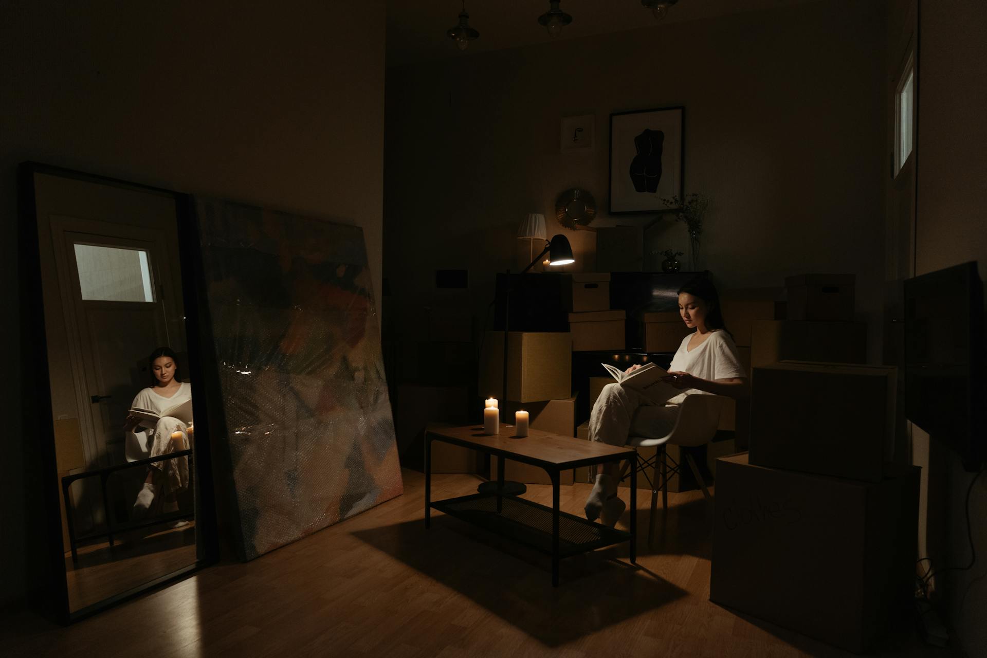 Woman reads by candlelight surrounded by moving boxes, creating a cozy, intimate ambiance.