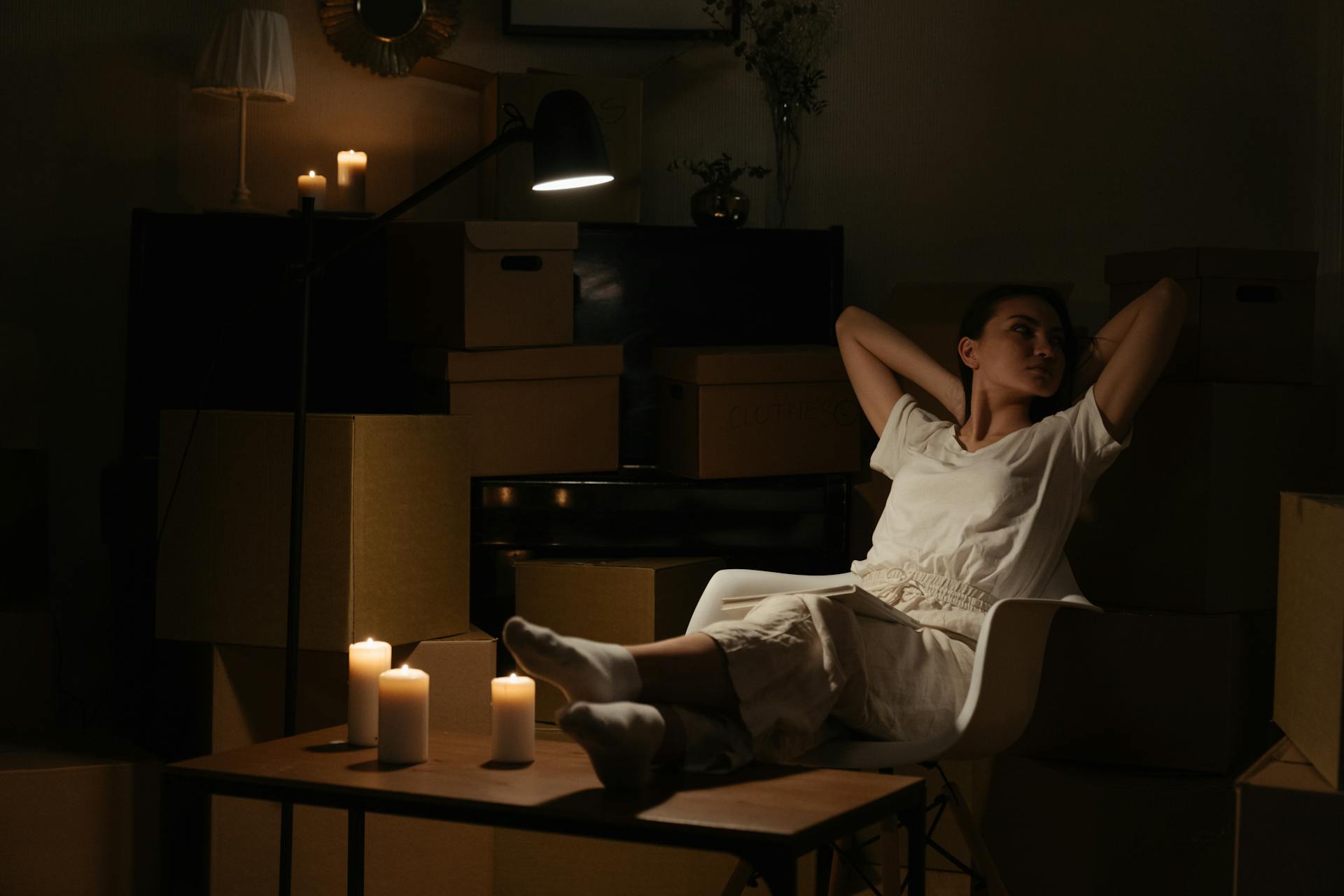 A woman peacefully sitting with candles and moving boxes, creating a serene atmosphere.