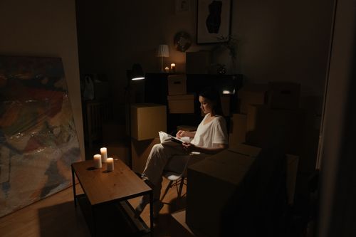 Free A woman reads by candlelight, surrounded by moving boxes, creating a serene atmosphere. Stock Photo