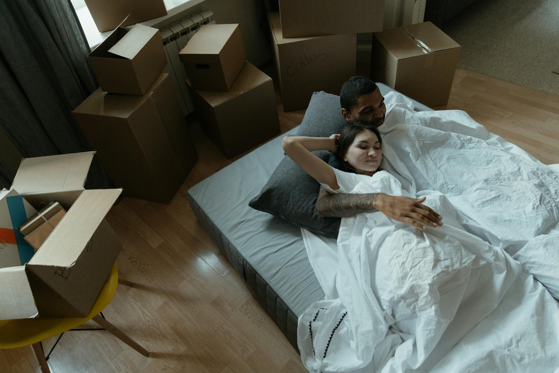 A couple relaxing on a mattress surrounded by moving boxes in their new home, embracing a fresh start.