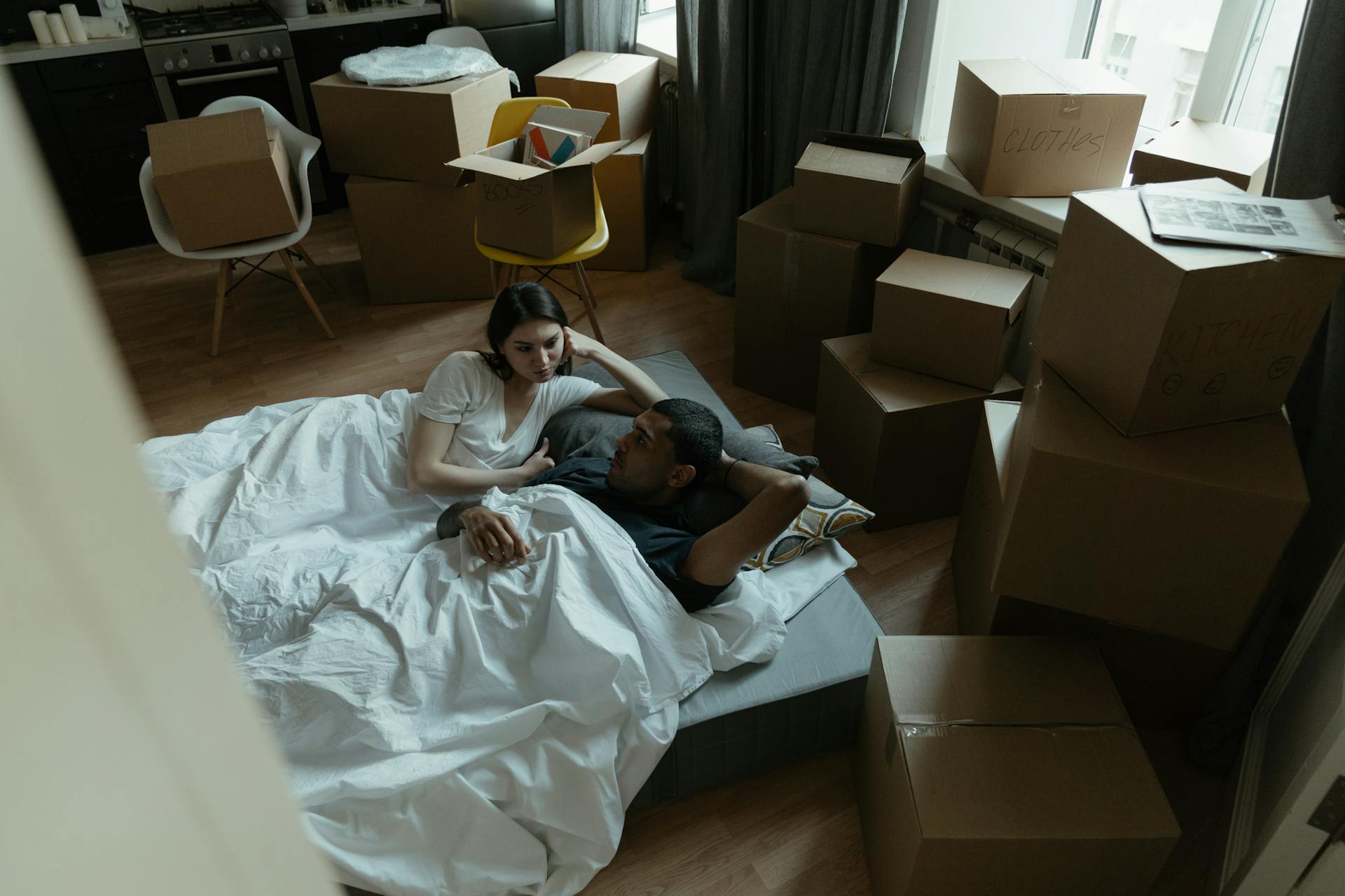 Couple lying in a new apartment surrounded by moving boxes, beginning a new life together.