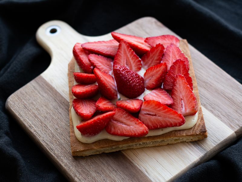 Delicious strawberry tart with cream on a wooden board, perfect for food photography.