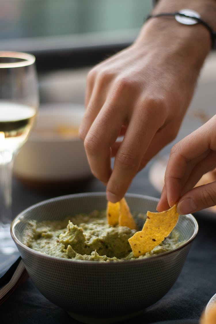 People Dipping Nacho Chips On Guacamole