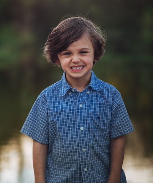 Free Positive little boy in stylish checkered shirt smiling while standing near lake in park and looking at camera Stock Photo