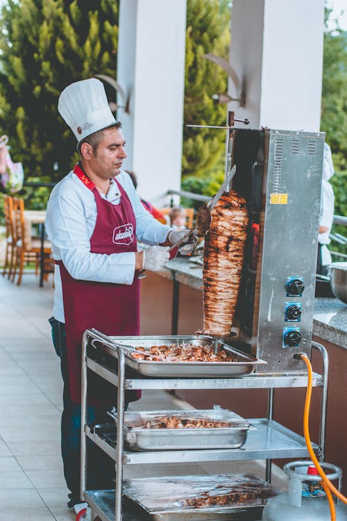 Ethnic male chef coking shawarma near counter in outdoor cafe