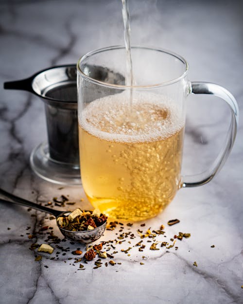 Free High angle of glass mug with pouring herbal tea placed on marble table near brewer Stock Photo