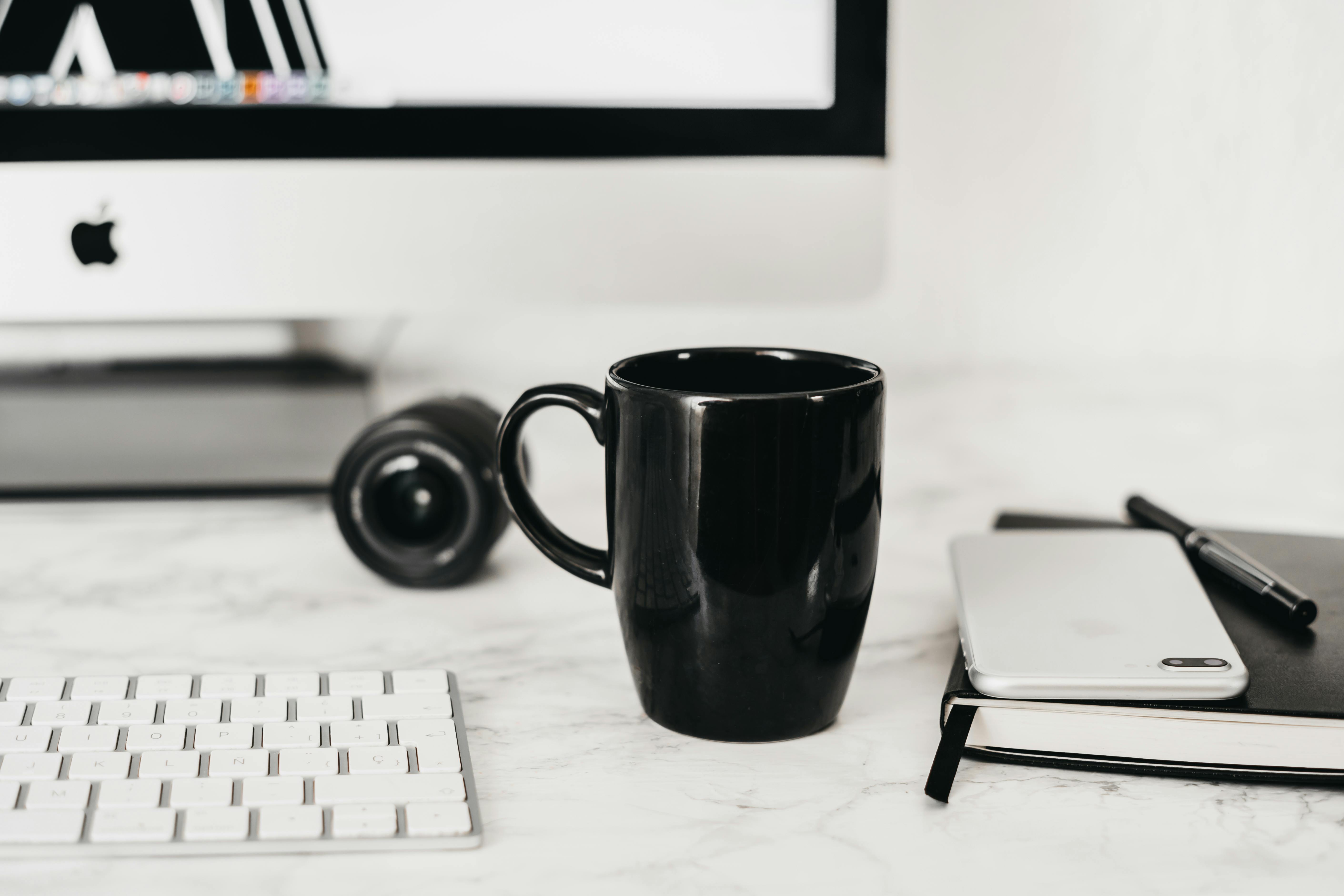Coffee cup placed on table near computer and notepad with smartphone
