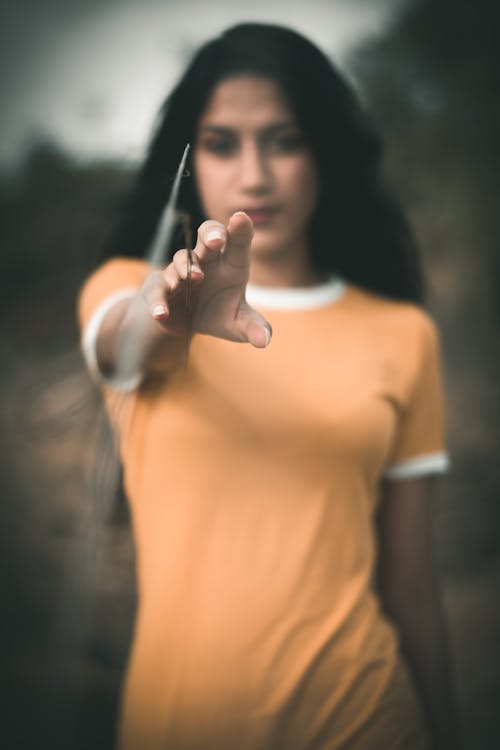 Pensive young ethnic female with long dark hair reaching out hand towards camera while standing in field in countryside