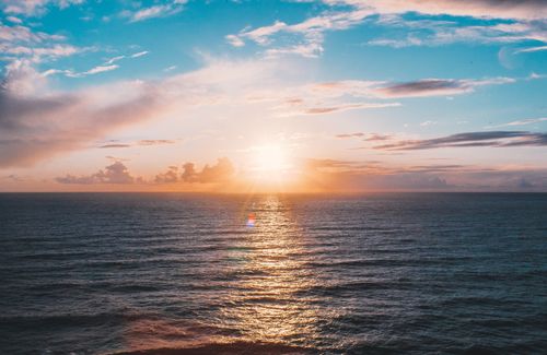 Free Picturesque scenery of sun shining over horizon and rippling wavy sea against cloudy blue sky at dusk Stock Photo