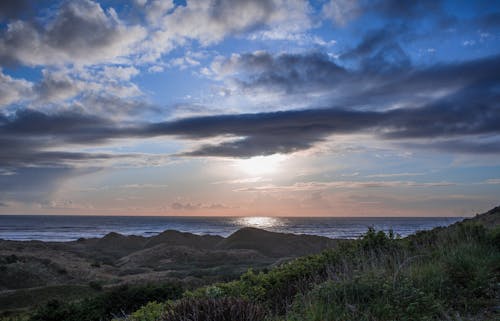 Sun shining through clouds over sea at dusk