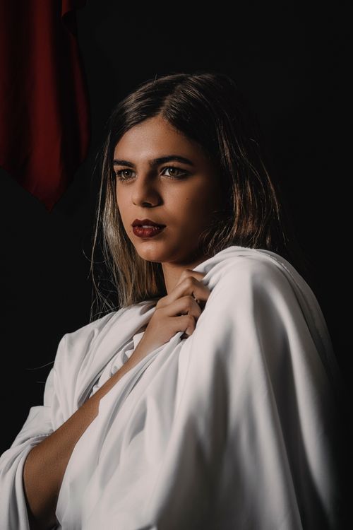 Free A captivating portrait of a woman holding a white fabric against a dark background, exuding elegance and poise. Stock Photo