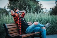 Man in Black and Red Plaid Dress Shirt and Blue Denim Jeans Sitting on Brown Wooden