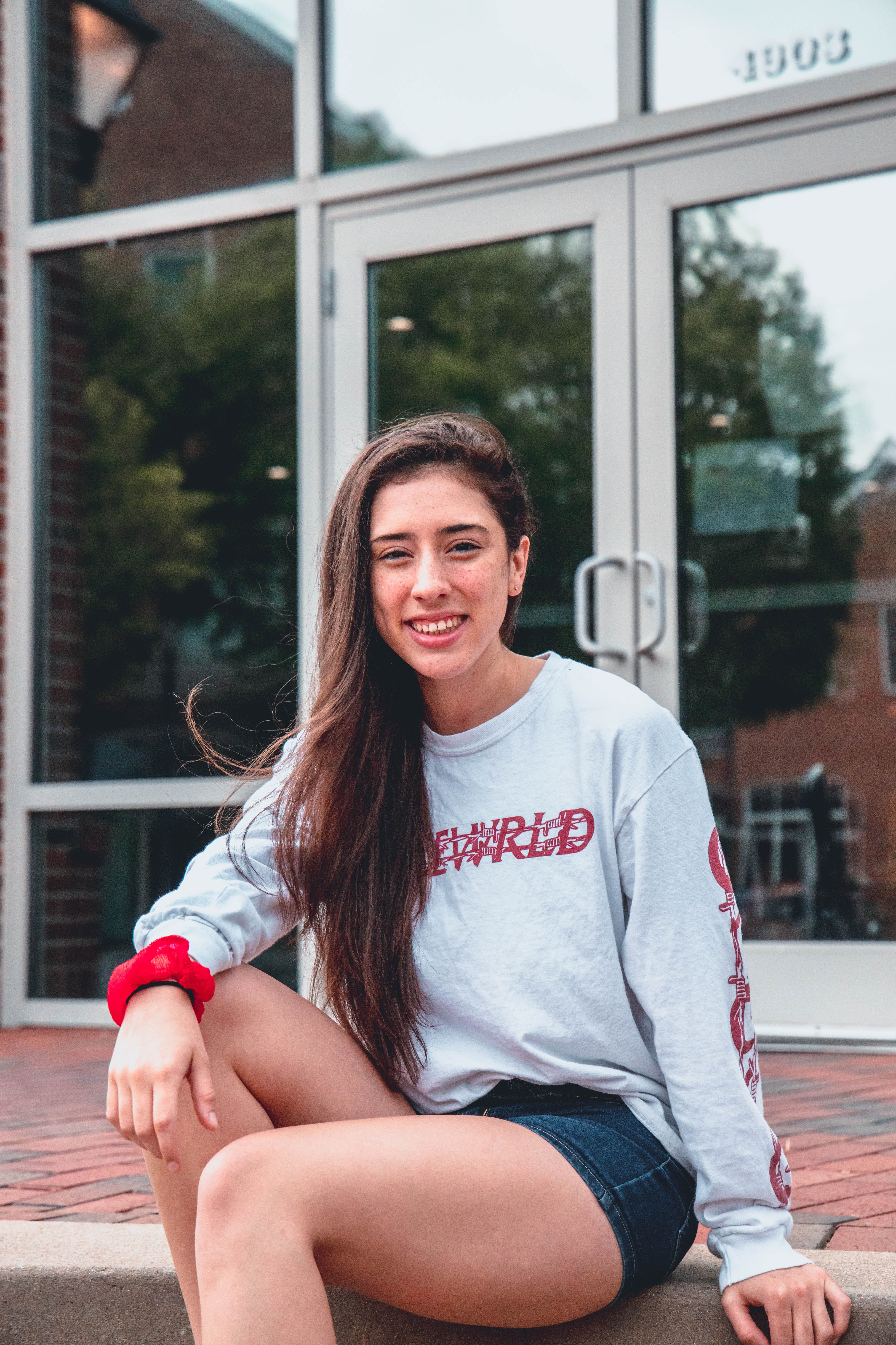 Delighted female sitting on paving stone near entrance of contemporary building while smiling and looking at camera during summer day