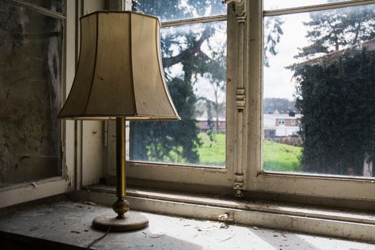 An old rustic lamp on a dusty windowsill in a vintage, abandoned house interior.