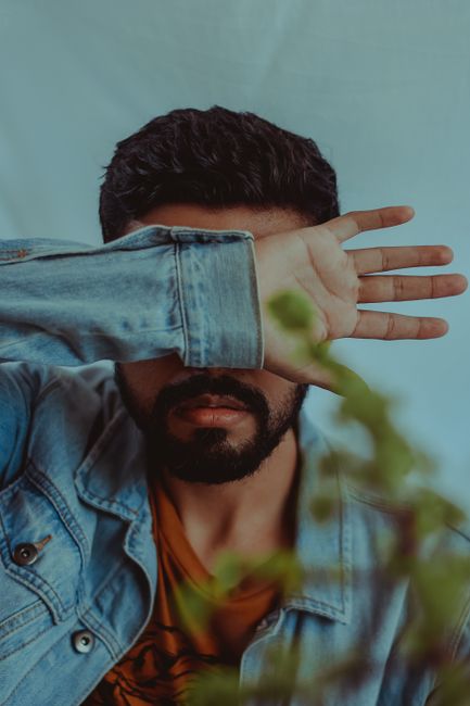 A man in a denim jacket covers his face with his hand, creating a mysterious vibe.
