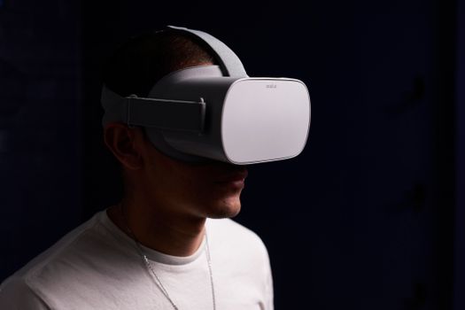 Close-up of a man wearing virtual reality goggles indoors in a dark setting.