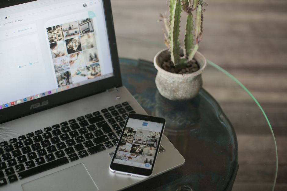 Un portátil y un smartphone mostrando aplicaciones de redes sociales al lado de un cactus en una mesa de vidrio.