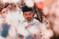 Stylish young queer male with earring and trendy hairstyle pulling up pullover sleeves in sunny nature