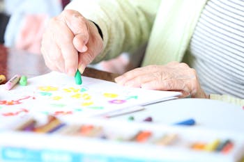 Crop senior patient drawing with crayon