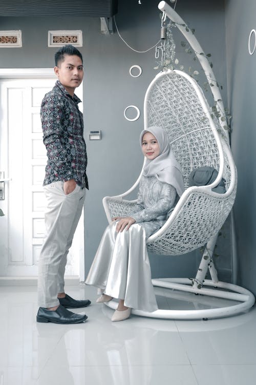 Full body Indian man standing near fiance in egg chair in creative gray design