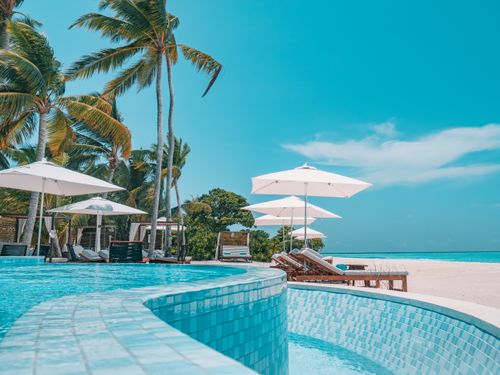 Free Tiled pool of exotic resort placed on white sandy beach with parasols and green palms Stock Photo