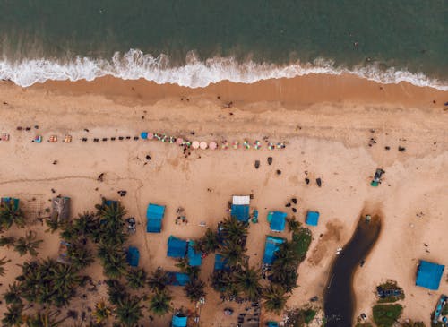 Drone view of resort with foamy waves and people chilling on sandy beach